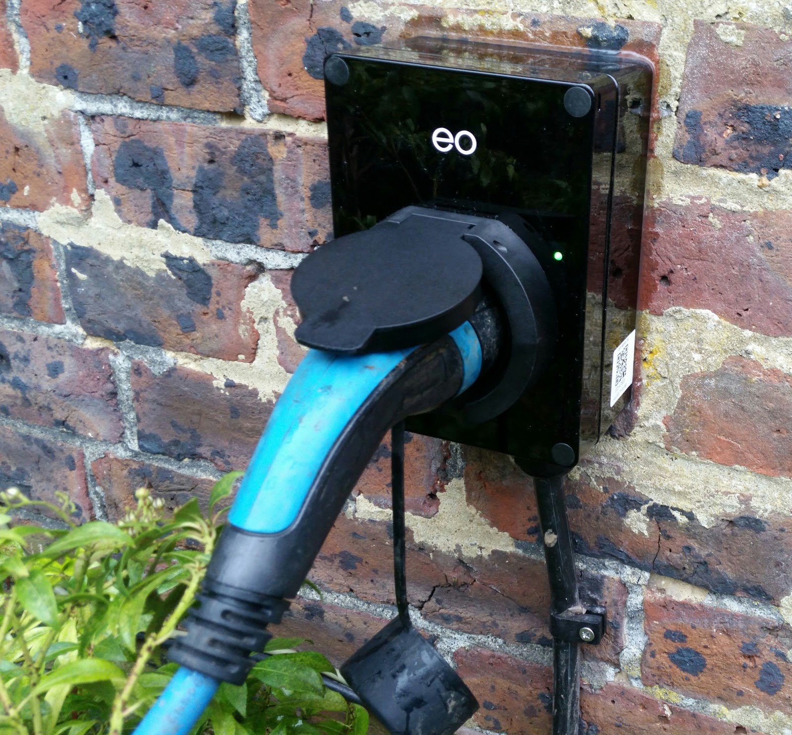 EO Mini charge point on brick, mid-charge with the connector plugged in — compact and weatherproof.