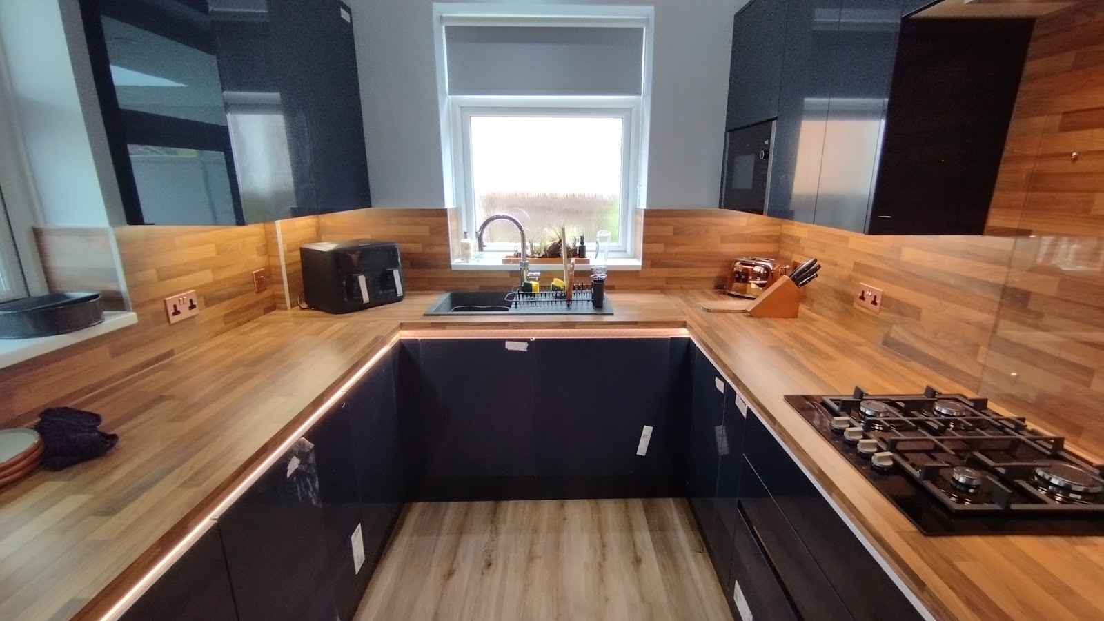 Under-cabinet LED strip lighting and a run of sockets across a wood-worktop kitchen.